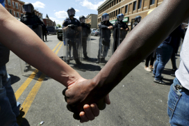 Members of the community hold hands in front of police officers in riot gear outside a recently looted and burned CVS store in Baltimore, Maryland, on April 28, 2015.  The day after rioters tore through Baltimore, the city's mayor was criticized on Tuesday for a slow police response to some of the worst U.S. urban unrest in years after the funeral of Freddie Gray, a 25-year-old black man who died in police custody. Maryland Governor Larry Hogan said he had called Mayor Stephanie Rawlings-Blake repeatedly Monday but that she held off calling in the National Guard until three hours after violence first erupted. Photo courtesy of REUTERS/Jim Bourg